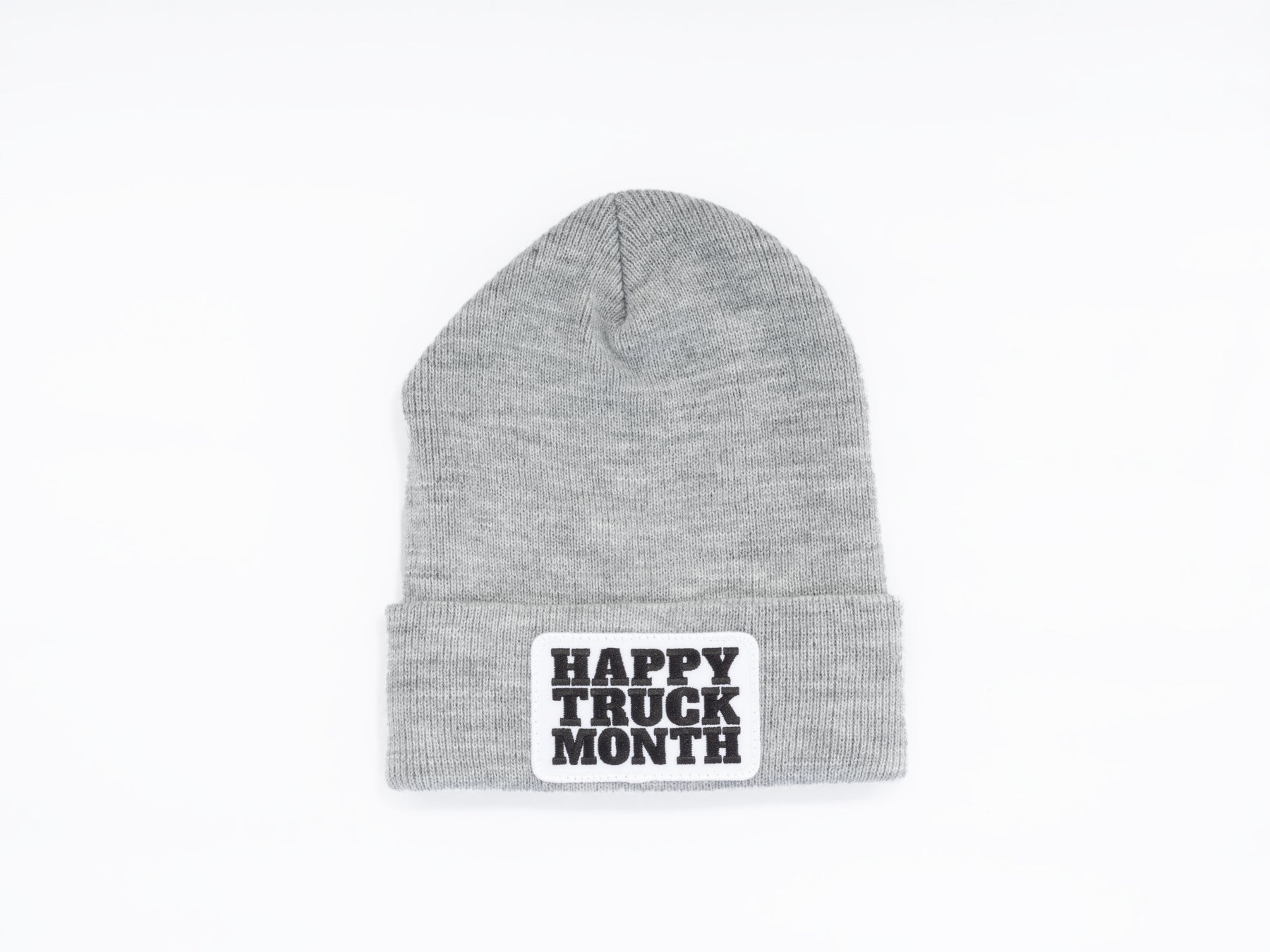 A gray knit beanie with a folded brim, featuring a white patch that reads HAPPY TRUCK MONTH in bold black letters. The beanie is displayed on a plain white background.