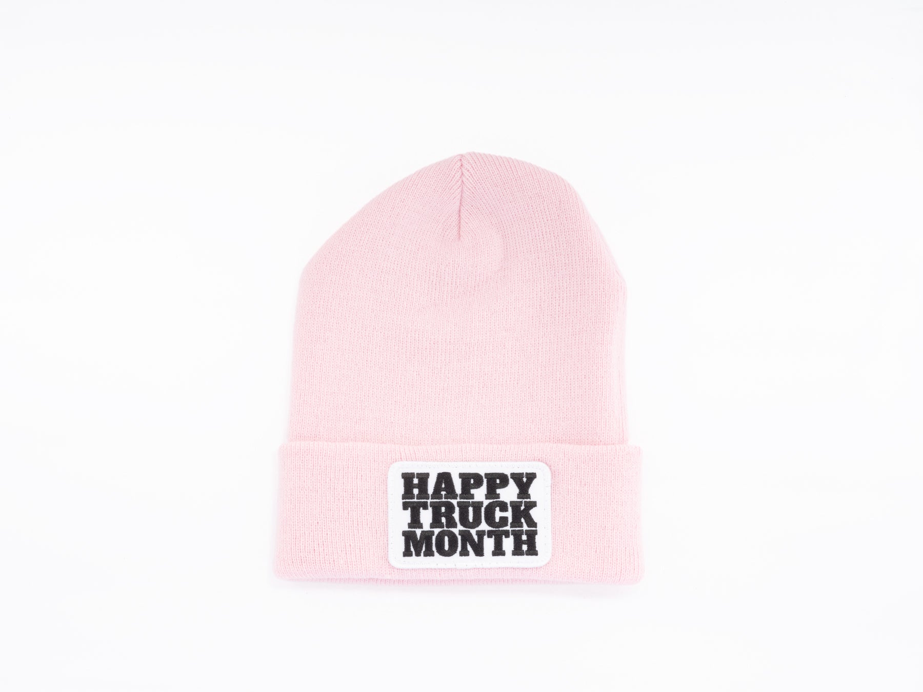 A light pink knit beanie with a folded brim featuring a white patch that has HAPPY TRUCK MONTH written in bold black letters.