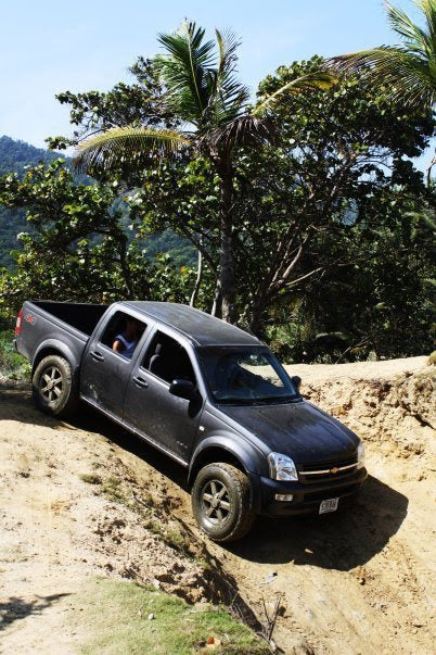 Black pickup truck on a dirt road with trees and mountains in the background