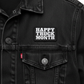 Close-up of a black denim trucker jacket with a rectangular black patch on the chest that reads 'HAPPY TRUCK MONTH' in white block letters. A small red tag is visible near the pocket, and the jacket has a dark washed denim texture.