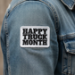 A rectangular embroidered patch reading “HAPPY TRUCK MONTH” in black letters on a white background, sewn onto the sleeve of a blue denim jacket.