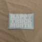 A rectangular light blue sticker or decal with the words 'HAPPY TRUCK MONTH' in large white block letters, placed on a beige fabric background.