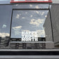 A white vinyl decal reading 'HAPPY TRUCK MONTH' applied to the rear window of a dark gray truck, with reflections of the sky and surrounding buildings visible on the glass.