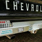 Close-up of the rear bumper and hitch area of a black Chevrolet truck outdoors on a leaf-covered ground. A Texas license plate, a 'Happy Truck Monthly' sticker, and part of the word 'CHEVROLET' are visible.